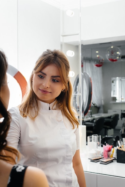 In einem schönen, modernen Schönheitssalon macht eine professionelle Make-up-Stylistin Make-up für ein junges Mädchen. Schönheit und Mode.