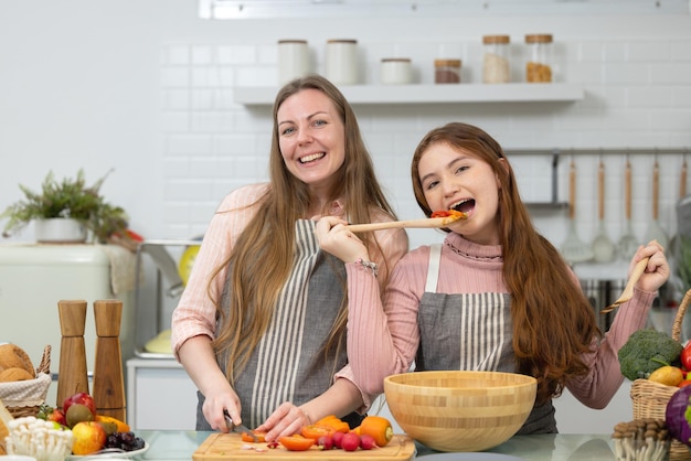 In einer weißen, makellosen, modernen Küche demonstrieren eine lächelnde Mutter und Tochter, wie man Gemüse zum Abendessen zubereitet