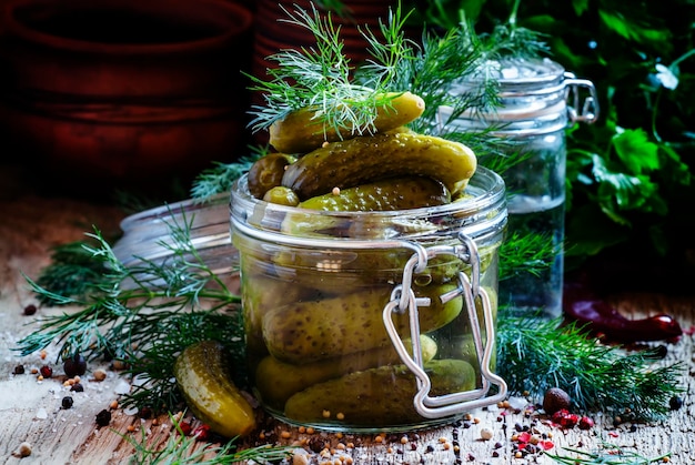 In Essig eingelegte kleine Gurkengurken in einem Glasgefäß mit Dillkräutern und -gewürzen auf einem selektiven Fokus des alten Holztisches Beschneidungspfad eingeschlossen