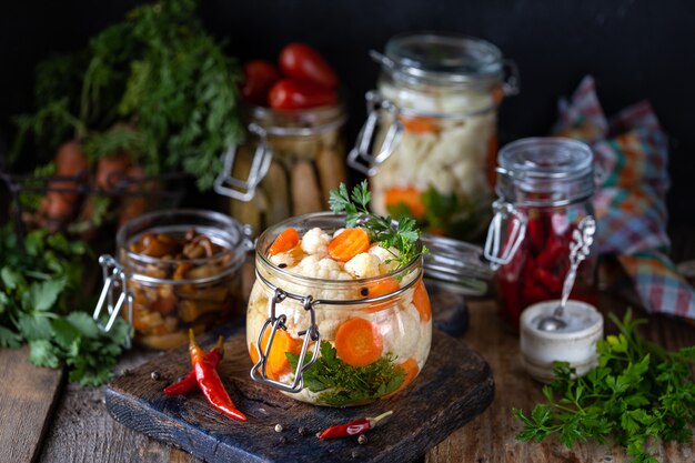 In Essig eingelegter Blumenkohl mit Karotten in einem Glasgefäß auf einem dunklen Holztisch.