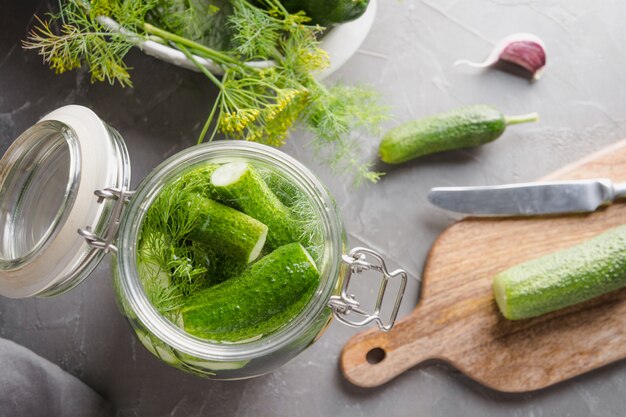 In Essig einlegen und Fermentationsgurke im Glasgefäß mit Dill und Knoblauch auf dunkelgrauer konkreter Tabelle.