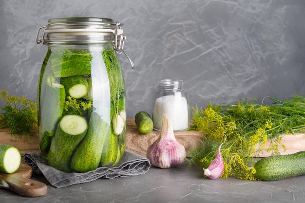 In Essig einlegen und Fermentationsgurke im Glasgefäß mit Dill und Knoblauch auf Grau.