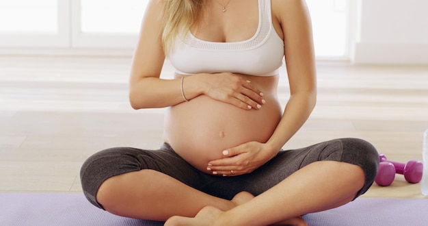 In guten Händen Schnappschuss einer nicht erkennbaren jungen schwangeren Frau, die ihren Babybauch reibt, während sie auf einer Yogamatte sitzt