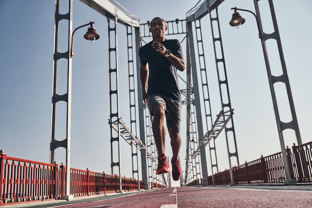 In guter Form. Voller Länge des jungen afrikanischen Mannes in Sportkleidung beim Joggen auf der Brücke im Freien