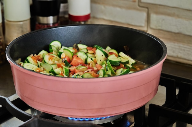 In halbe Ringe geschnittene Zucchini mit Tomaten werden in der Pfanne auf dem Gasherd gebraten