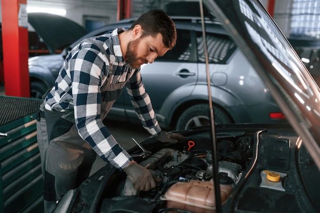 In Handschuhen repariert er ein Auto. Ein Mann in Uniform arbeitet im Autosalon