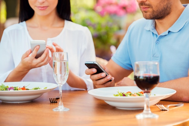 In ihren getrennten Welten. Nahaufnahme eines jungen Paares, das etwas auf ihren Smartphones eintippt, während sie sich gemeinsam im Restaurant im Freien entspannen?