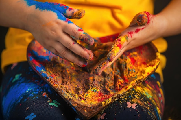 in Kinderhänden ein herzförmiger Holzteller mit bunten Holi-Blüten