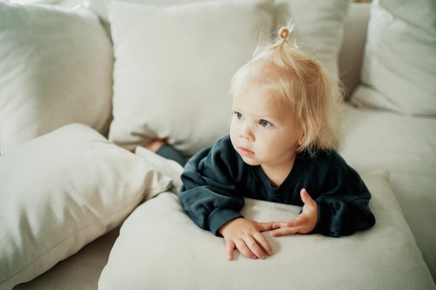 In Kinderkleidung gekleidet Verbringt Zeit zu Hause auf der Couch Nettes kleines blondes Mädchen