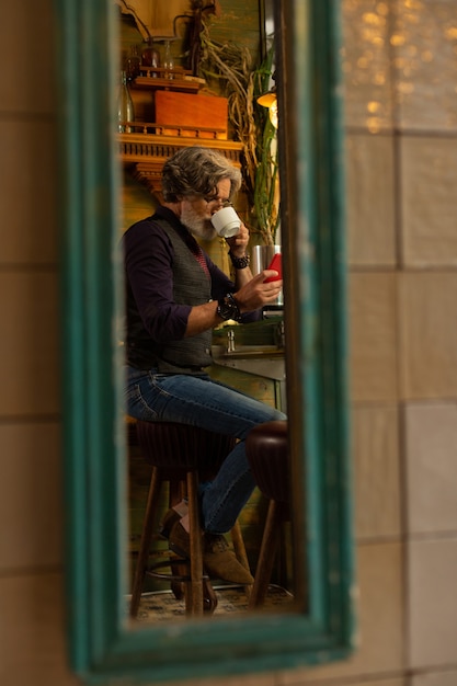 In Kontakt zu bleiben. Konzentrierter Mann, der seiner Frau eine Nachricht schreibt, während er im Café sitzt und Kaffee trinkt.