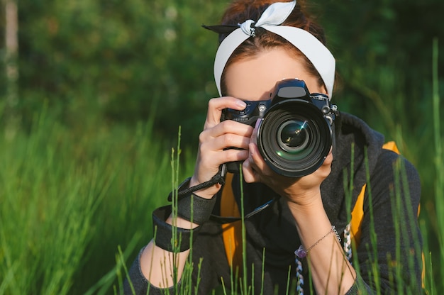 In Nahaufnahme fotografiert das Mädchen mit einer professionellen Foto-Video-Kamera. Vor dem Hintergrund grüner Natur und Wald.