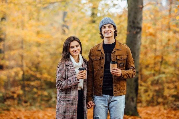 In Schals verliebtes Paar sitzt im Park und hält Tassen Tee oder Kaffee