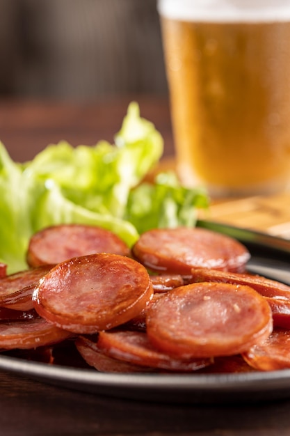 In Scheiben geschnittene gebratene Peperoniwurst mit einem Glas Bier auf dem Tisch