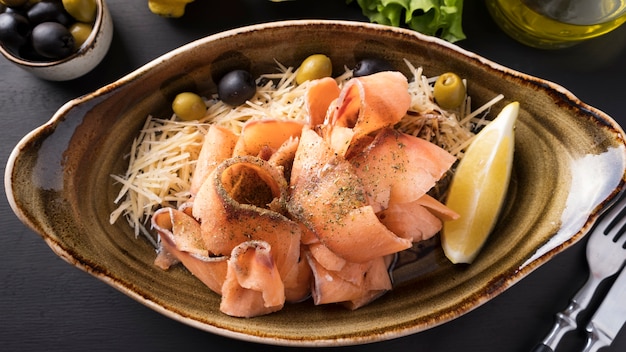 In Scheiben geschnittene gefrorene rohe Lachs-Stroganina auf einem Teller mit Käse, Oliven und Zitrone. In Scheiben geschnittener gefrorener Fisch. Draufsicht