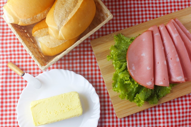 In Scheiben geschnittene Mortadella auf Schneidebrett, Brot und Butter in der Küche mit karierter Tischdecke