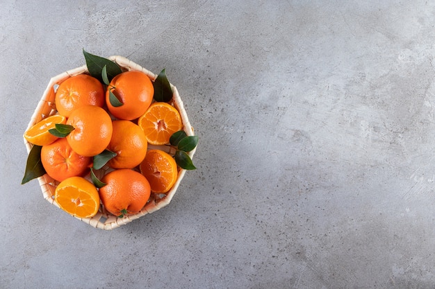 In Scheiben geschnittene und ganze frische Orangenfrüchte mit Blättern in einem Weidenkorb