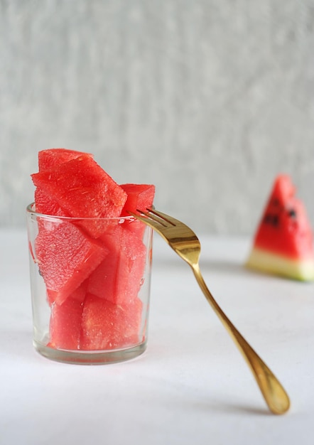 In Scheiben geschnittene Wassermelone liegt in einem transparenten Glas. In der Nähe gibt es eine goldene Gabel und eine Scheibe Wassermelone