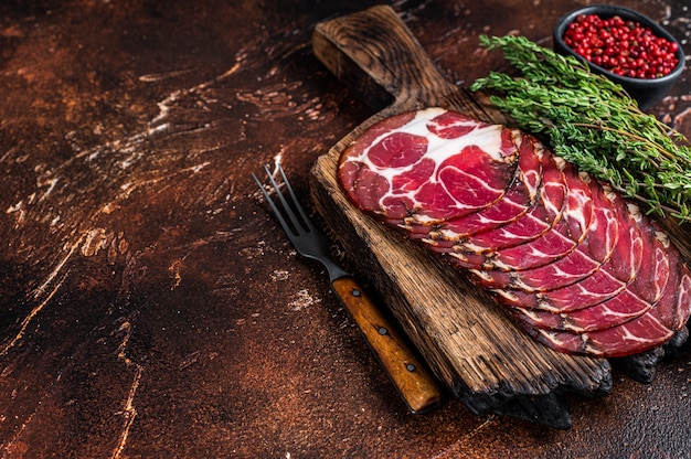 In Scheiben geschnittener Coppa-Schinken auf Holzbrett mit Thymian. Dunkler Hintergrund. Draufsicht. Speicherplatz kopieren.