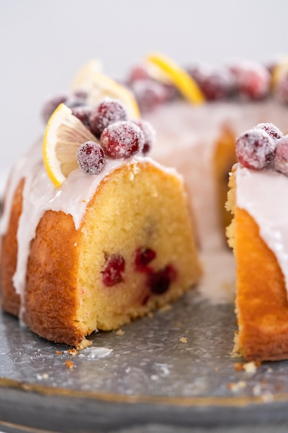 In Scheiben geschnittener Zitronen-Cranberry-Bundt-Kuchen, dekoriert mit Zuckerpreiselbeeren und Zitronenschnitzen auf einem Tortenständer.