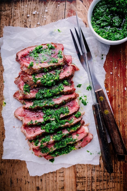 In Scheiben geschnittenes gegrilltes Rindersteak mit grüner Chimichurri-Sauce auf Holzhintergrund