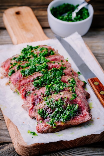 In Scheiben geschnittenes gegrilltes Rindersteak mit grüner Chimichurri-Sauce auf Holzhintergrund