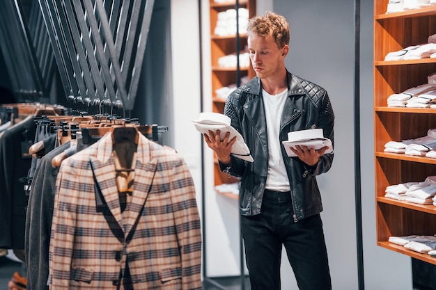 In schöner schwarzer Jacke Junger Mann im modernen Laden mit neuer Kleidung Elegante teure Kleidung für Männer