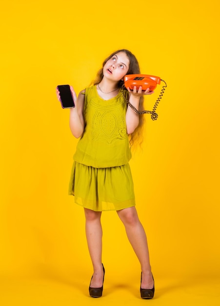 In Shop-Gespräch und Kommunikation Teenager-Mädchen mit Retro-Telefon und Smartphone-Kind Vintage-Mode glückliche Kindheit süßes Kind auf gelbem Hintergrund neue Technologie im modernen Leben
