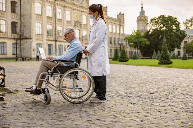 In voller Länge Aufnahme einer jungen Ärztin, die sich um einen älteren Patienten im Rollstuhl kümmert