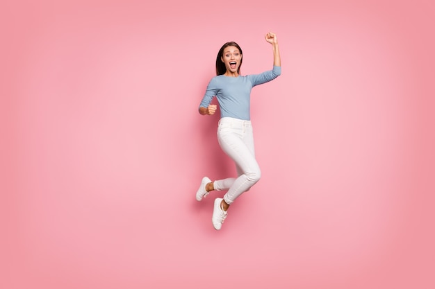 In voller Länge gedrehtes Körpergrößenfoto des fröhlichen schreienden schreienden positiven Mädchens, das Aufregung auf Gesicht ausdrückt, das Faust in blauem Pullover lokalisiertem pastellfarbenem Hintergrund macht