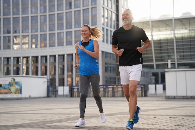 In voller Länge geschossen von motivierten Paaren mittleren Alters und einer Frau in Sportbekleidung, die zusammen in laufen