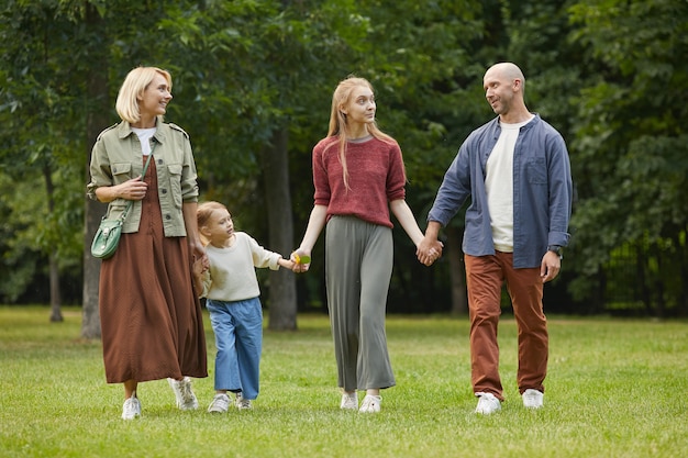 In voller Länge Porträt der modernen Familie mit zwei Kindern, die Hände beim Gehen auf grünem Gras im Freien halten