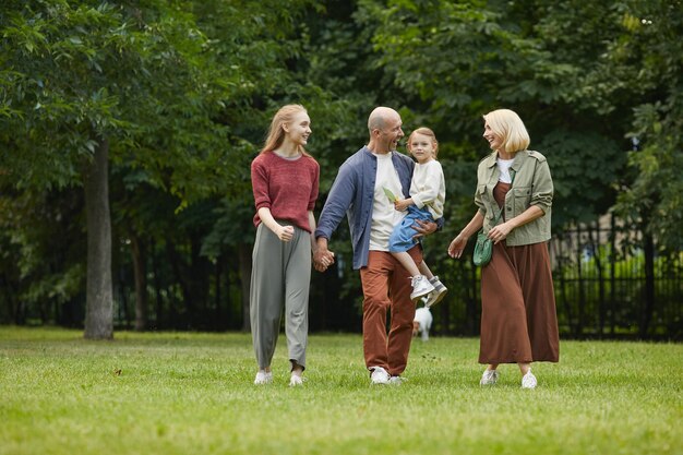 In voller Länge Porträt einer sorglosen Familie mit zwei Töchtern, die draußen auf grünem Gras stehen, während sie zusammen im Park spazieren gehen