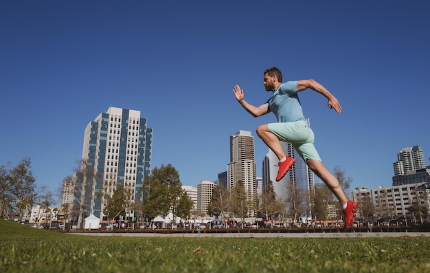In voller Länge von einem gesunden Mann, der im Freien in der Nähe der Skyline der Stadt läuft und sprintet, männlicher urbaner Läufer Dynami