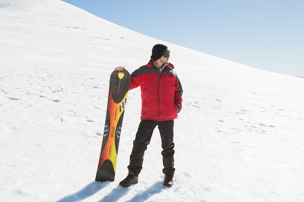 In voller Länge von einem Mann mit dem Skibrett, das weg auf Schnee schaut