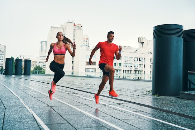 In voller Länge von zwei jungen Leuten in Sportkleidung, die springen und joggen, während sie im Freien auf der Stadtstraße trainieren exercising