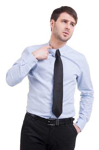 Incertidumbre. Hombre joven frustrado en camisa y corbata sosteniendo el pelo de iones de la mano mientras está de pie aislado en blanco