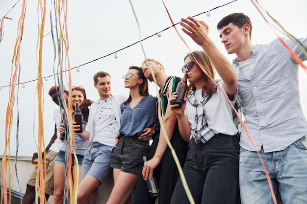 Inclinando-se na beira do telhado com enfeites Grupo de jovens em roupas casuais fazem uma festa juntos durante o dia