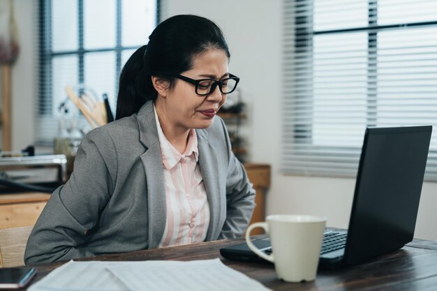 la incómoda trabajadora coreana que presiona su vientre tiene un dolor repentino en el estómago mientras teletrabaja en el apartamento. una dama asiática con dolor por la menstruación no puede continuar trabajando en el proyecto.