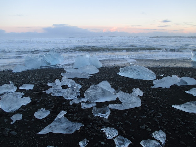Incontáveis icebergs na praia de areia preta contra o céu do sol, sul da Islândia