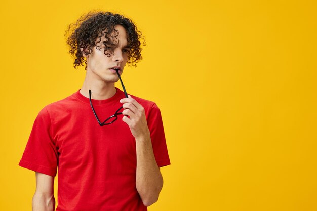 Incrédulo miope jovem estudante de camisa vermelha segurar óculos engraçados em dentes posando isolado em fundo de estúdio amarelo a melhor oferta com lugar grátis para publicidade conceito de faculdade de educação