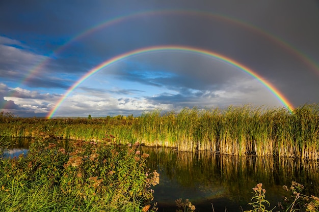 Increíble arco iris doble sobre el pequeño río rural