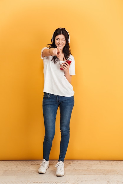 Increíble feliz linda joven mujer bonita escuchando música con auriculares apuntando.