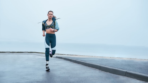 Increíble fuerte mujer discapacitada en ropa deportiva está corriendo al aire libre cerca del mar