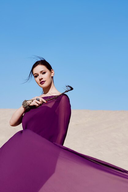 Increíble hermosa mujer morena con la pluma de pavo real en tela morada en el desierto