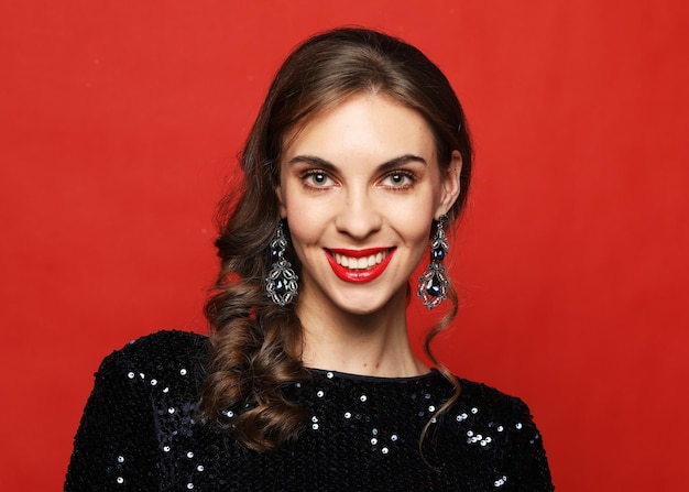 Increíble mujer de lujo en elegante vestido de fiesta posando sobre fondo rojo.