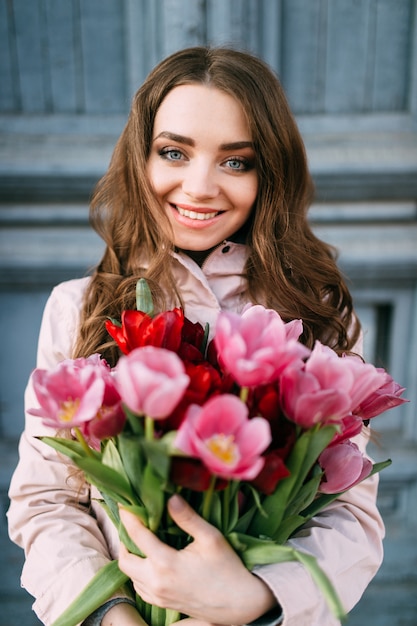 increíble mujer morena de pie delante de la vieja puerta azul con un ramo de tulipanes.