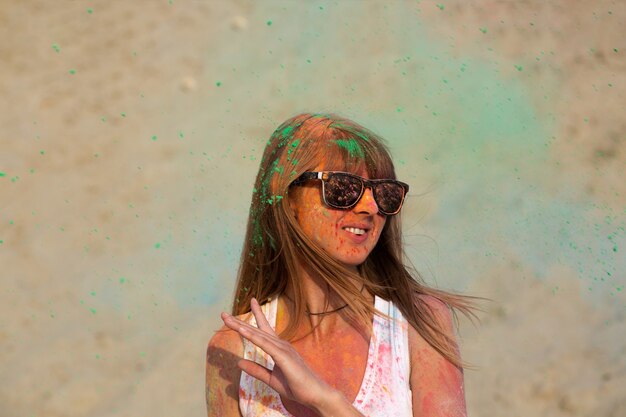 Increíble mujer rubia con gafas jugando con pintura verde seca Holi en el desierto