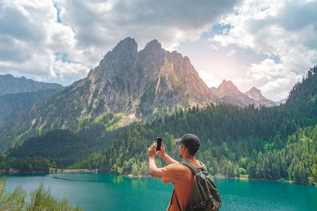 Foto increíble paisaje con hombre tomando fotos con camisa naranja de pie en la cima de una montaña verde