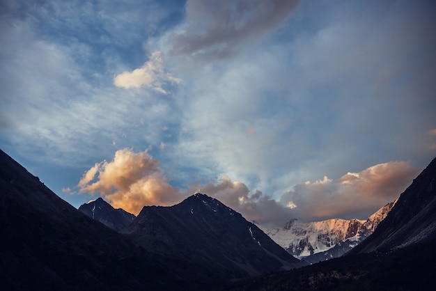 Increíble paisaje vívido del atardecer con impresionantes siluetas de montañas y nubes naranjas.