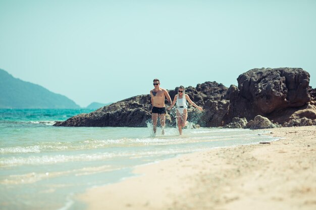 Increíble pareja joven corre en la playa de la mano del hombre en pantalones de baño y su novia